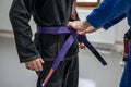 BJJ brazilian jui jutsu belt promotion close up on hands of unknown instructor black belt professor tie up purple belt on waist of