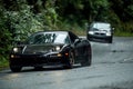 Black Acura NSX driving on a road in the woods on a rainy day with BMW car in the background