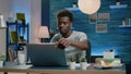 Black adult working from home with laptop and coffee at desk