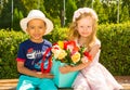 Black african american boy kid gives flowers to girl child on birthday. Little adorable children in park.