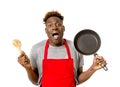 Black afro american man home cook in chef apron cooking pan and spoon lost and overworked Royalty Free Stock Photo