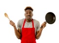 Black afro american man home cook in chef apron cooking pan and spoon lost and overworked Royalty Free Stock Photo