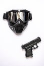 A black airsoft mask along with a mantle gun on a smooth white surface