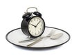 Black alarm clock with fork and knife on the plate. Isolated on white. Time to eat. Weight loss or diet concept Royalty Free Stock Photo