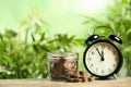 Black alarm clock, glass jar and coins on table. Money savings Royalty Free Stock Photo