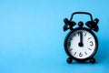 Black alarm clock isolated on blue background. The clock set at 12pm. Copy space and time concept Royalty Free Stock Photo