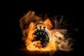 A black alarm clock with large numbers on a dark background surrounded by burning hot particles