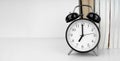 Black alarm clock next to the books on the white table Royalty Free Stock Photo