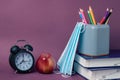 Black alarm clock, red apple, medical masks and school supplies on a purple background