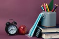 Black alarm clock, red apple, medical masks and school supplies on a purple background.