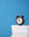 Black alarm clock on stack of books on blue background, mockup design Royalty Free Stock Photo