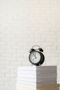Black alarm clock on stack of books on white brick wall background Royalty Free Stock Photo