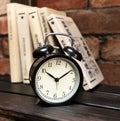 Black alarm clock on a wooden shelf in the background of the books and brick wall Royalty Free Stock Photo