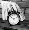 Black alarm clock on a wooden shelf in the background of the books and brick wall Royalty Free Stock Photo