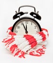 The black alarm clock is wrapped in a warm knitted red and white scarf. Time, about twelve.