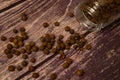 Black allspice scattered on a wooden background and a glass spice jar with black pepper lying on its side. Close up
