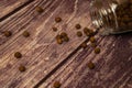 Black allspice scattered on a wooden background and a glass spice jar with black pepper lying on its side. Close up