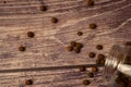 Black allspice scattered on a wooden background and a glass spice jar with black pepper lying on its side. Close up