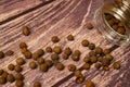 Black allspice scattered on a wooden background and a glass spice jar with black pepper lying on its side. Close up