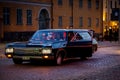 Black American car with greasers cruising at a city street at night.