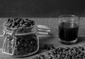 Black american coffee in glass with coffee beans in glass jar on rustic wooden table and dark background.Black and white Royalty Free Stock Photo