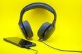 Black android smartphone with headphones on yellow background