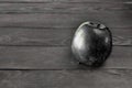 Black apple lies on a gray wooden table against