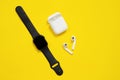 Black AppleWatch and white AirPods with box on bright yellow background. Isolated, copy space for text or advertisement. Royalty Free Stock Photo