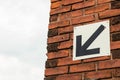 Black arrow sign pointing downwards and to the left. On red brick wall. Royalty Free Stock Photo