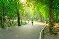 A black asfalt concrete jogging track in a public park, two people wearing yellow and green T shirt running on curve shape way