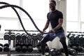 Black athlete doing battle rope exercise at crossfit gym