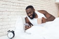 Black, awakened man drinks coffee in bed browsing