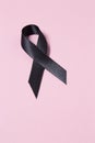 A black awareness ribbon isolated on pink background