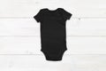 Black baby onesie mockup on white wood background Royalty Free Stock Photo