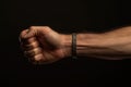 On black background close up muscular arm of caucasian man clench fist. On the wrist handcuff bracelet, male strength