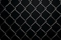 Black background enhances the grid pattern of chain link mesh fence