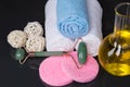 On a black background, items for spa treatments, a towel wrapped in a roll, fragrance oil, facial cleansing sponges and a natural