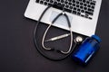on a black background lies a laptop on the keyboard which has a stethoscope, scissors, thermometer, pills in a bottle Royalty Free Stock Photo