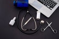 on a black background lies a laptop on the keyboard which has a stethoscope, scissors, thermometer, pills in a bottle Royalty Free Stock Photo