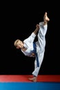 On a black background and red mat the boy beat blow leg mawashi geriMawashi-geri athlete in performing in white karategi on a bla