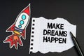 On a black background, a rocket, a marker and paper with the inscription - MAKE DREAMS HAPPEN
