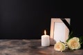 Blank funeral frame, candle and flowers on table against black background Royalty Free Stock Photo