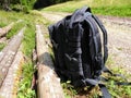 Black backpack on hiker trail, storage near logs on path.