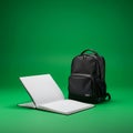 A black backpack and an open, blank hardcover book are placed against a solid green Royalty Free Stock Photo