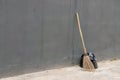 A black bag of garbage and old broom against a gray wall