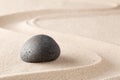 Black basalt stone on sandy beach sand with line pattern