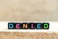 Black bead with letter in word denied on wood background