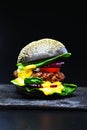Black beef burger with flowing melted cheese on a black background. Royalty Free Stock Photo