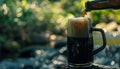 Black beer pouring into mug in nature background