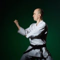 With a black belt, the athlete does formal karate exercises on a dark green background Royalty Free Stock Photo